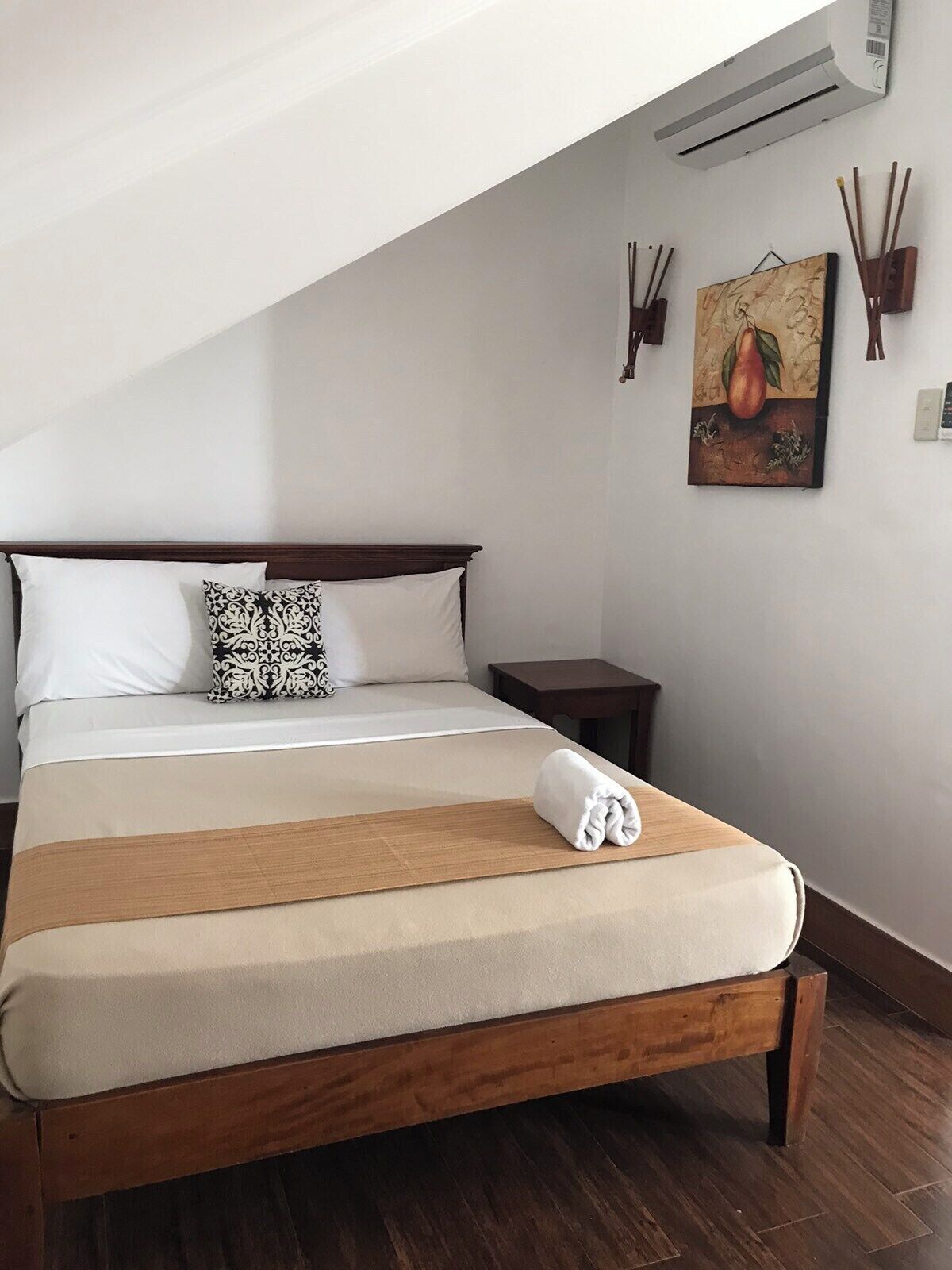 A neatly made bed with a wooden headboard, a small bedside table, and a wall-mounted air conditioner.