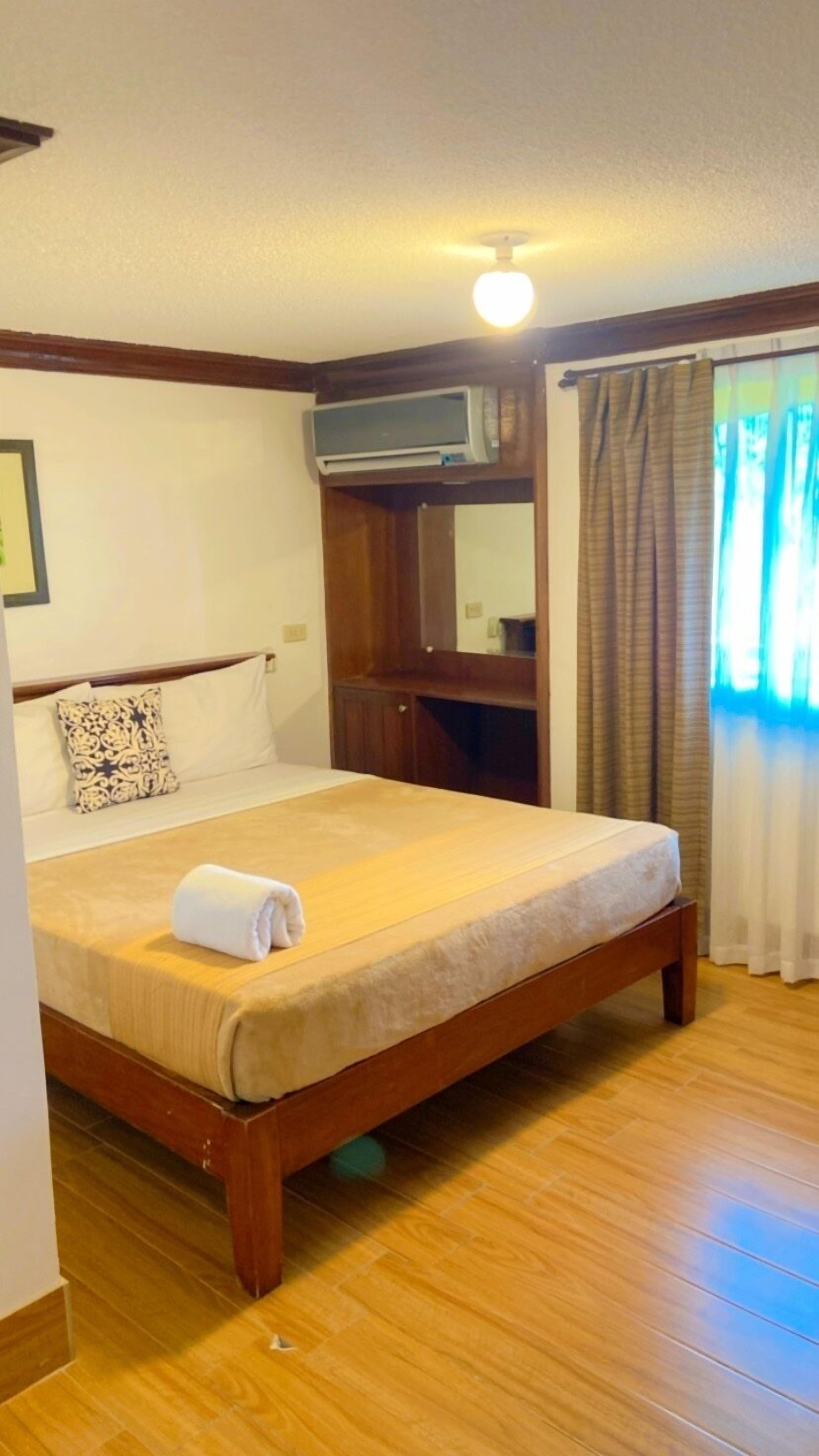 A neatly made bed with a rolled towel, wooden headboard, and a small bedside table.