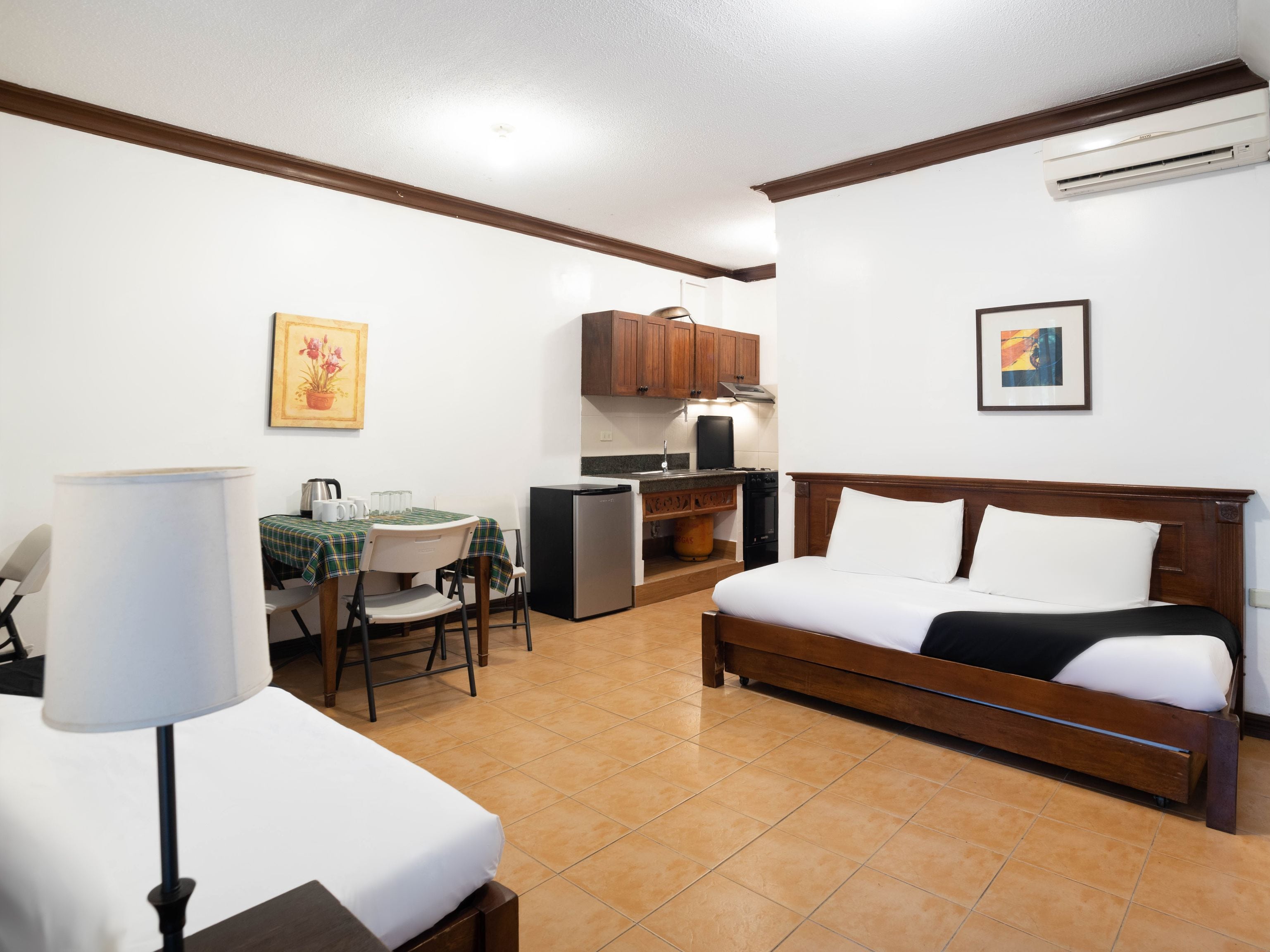 A compact room with a bed, a small table with chairs, a kitchenette, and a ceiling fan.