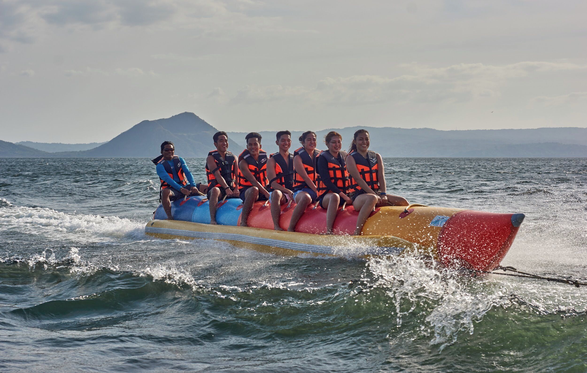 A group of people on a watercraft with life jackets, surrounded by water and distant mountains.