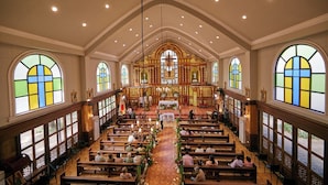 Ein Kircheninneres mit in Reihen angeordneten Kirchenbänken, einem zentralen Altar und farbigen Glasfenstern.
