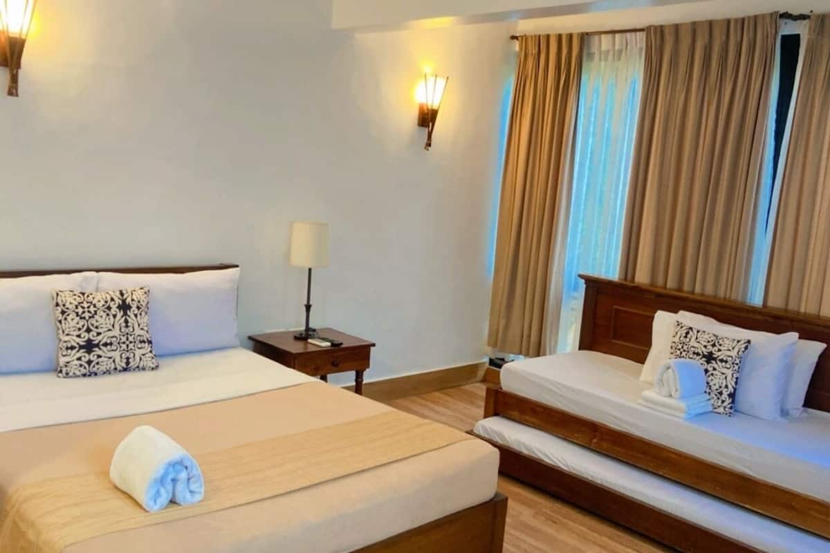 A hotel room with two beds, a nightstand, a lamp, and a window with curtains.
