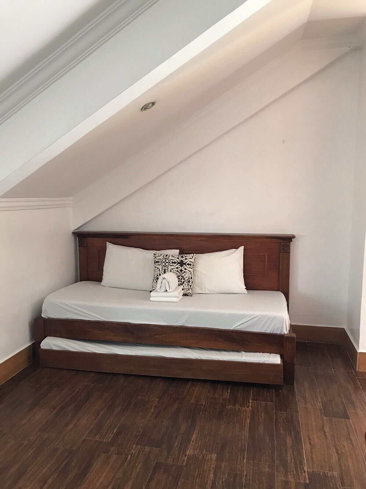 A bedroom with a sloped ceiling, a wooden bed frame, white bedding, and a patterned pillow.