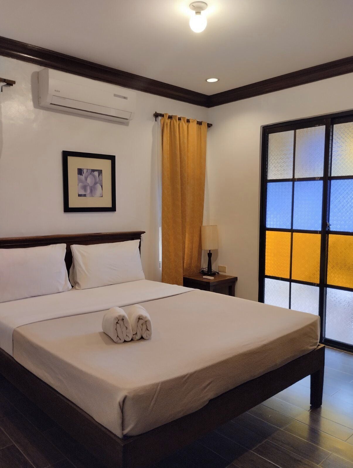 Habitación de hotel con una cama grande, una mesita de noche con lámpara, un cuadro en la pared y una ventana con vistas.