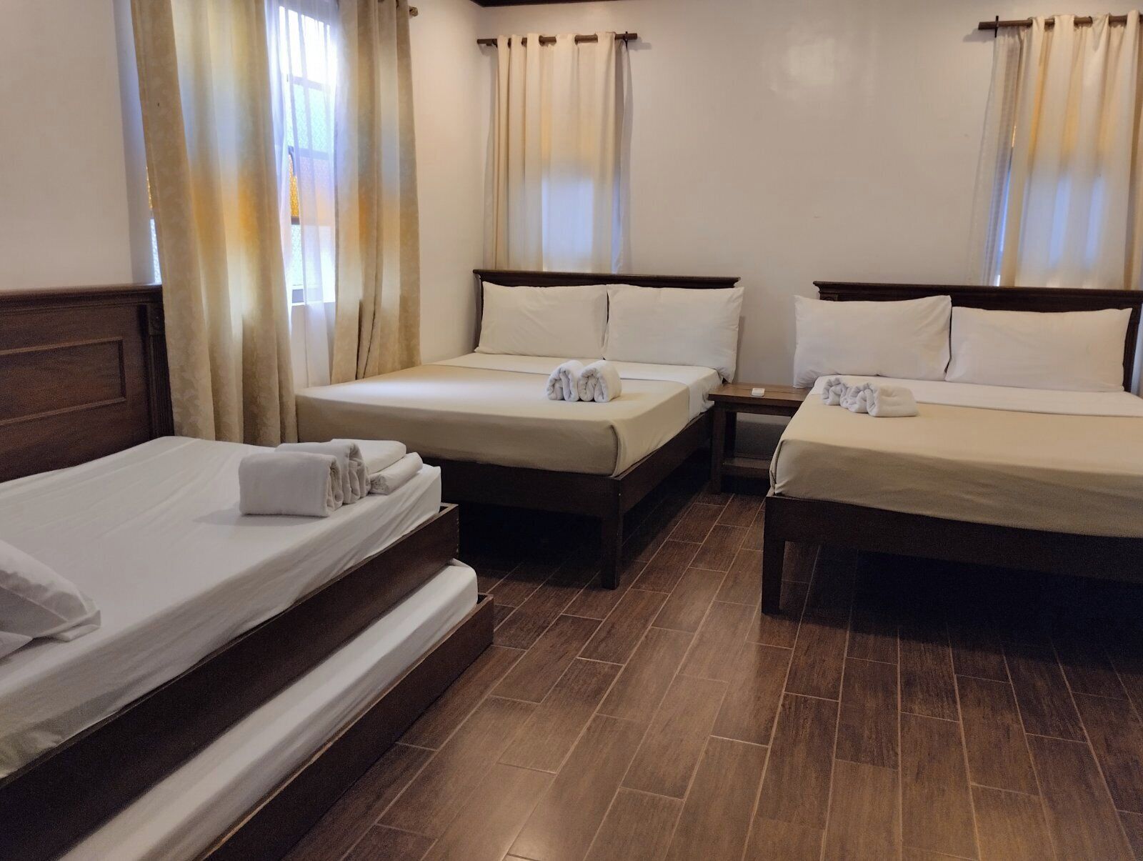 Habitación de hotel con dos camas individuales, una cama más grande y un cabecero de madera.