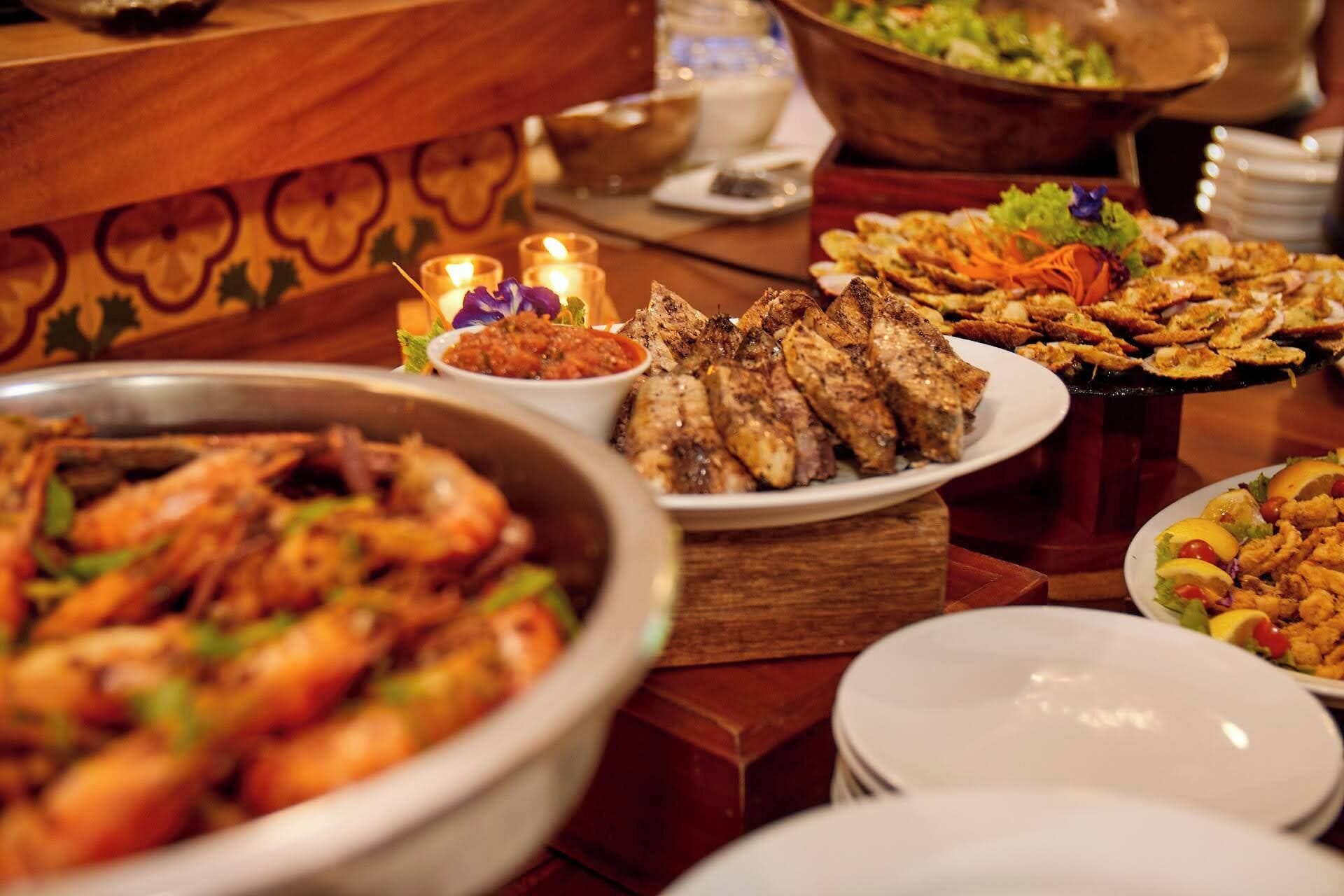 Un bufé con diversos platos, incluyendo carnes a la parrilla, mariscos y ensaladas.
