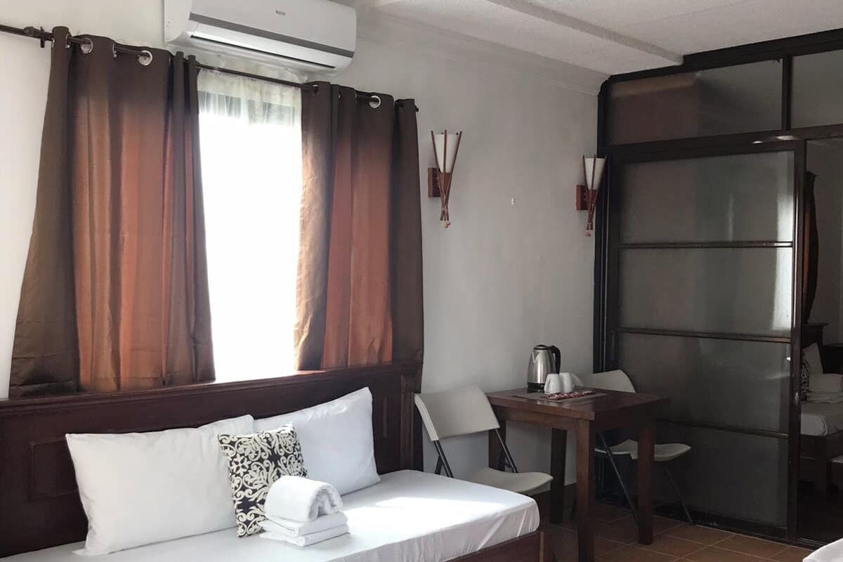 A hotel room with a bed, a desk, a chair, an air conditioning unit, and a sliding glass door.