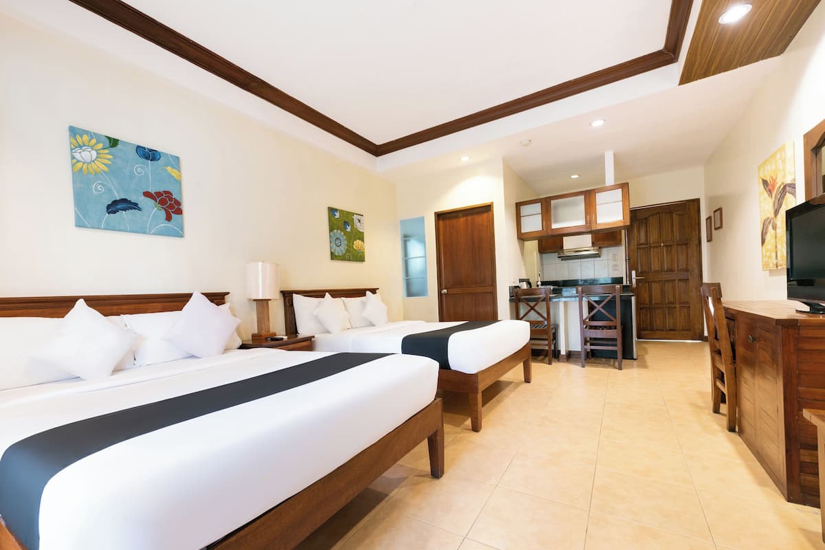 A hotel room with two beds, a kitchenette, wooden furniture, and artwork on the walls.