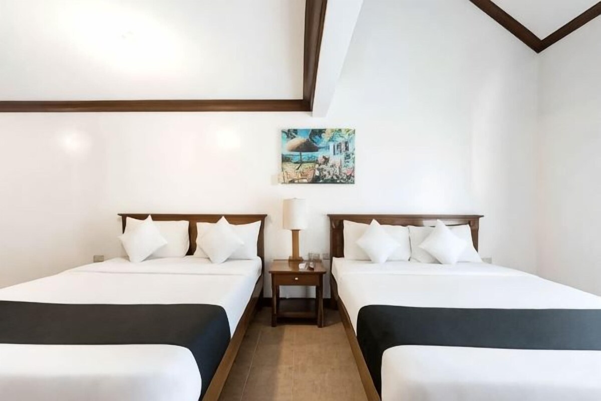 A hotel room with two beds, a nightstand, a lamp, and a painting on the wall.