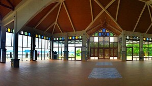 Ein geräumiger Saal mit hoher Decke und großen Fenstern, mit einem zentralen Buntglasfenster und Holzbalken.