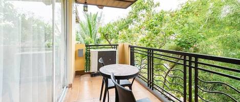 Un balcone con tavolo e sedie, una panca, un piccolo riscaldatore e vista sul verde.