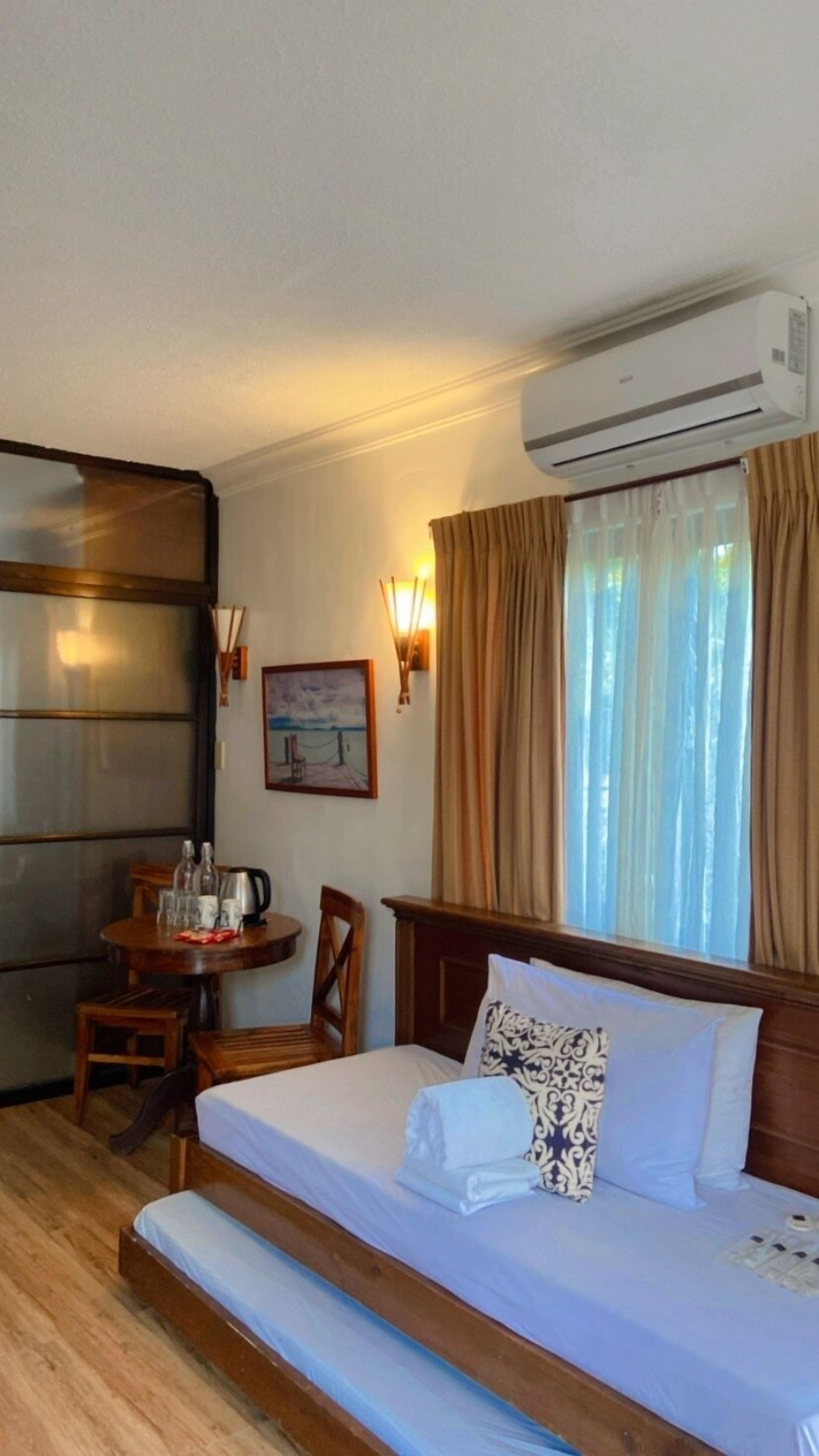 Una habitación de hotel con una cama, un escritorio con una silla, un cuadro en la pared y un equipo de aire acondicionado.