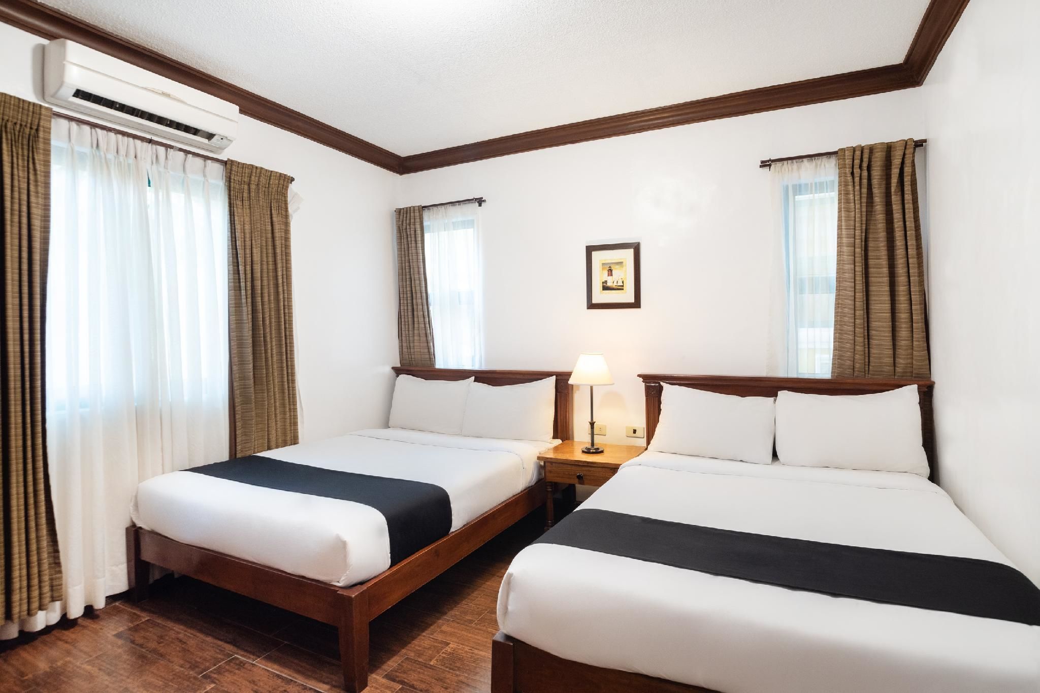 A hotel room with two beds, wooden headboards, a nightstand with a lamp, and an air conditioning unit.