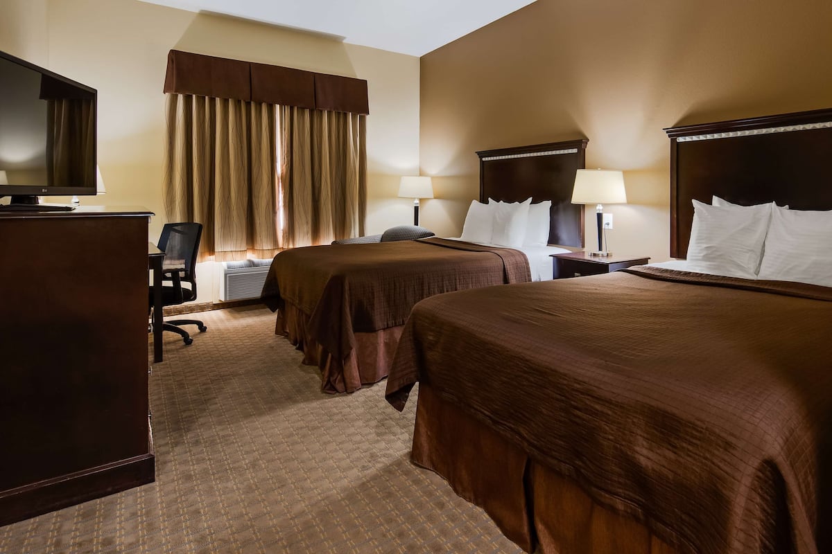 A hotel room with two beds, a desk, a chair, a TV, and a window with curtains.