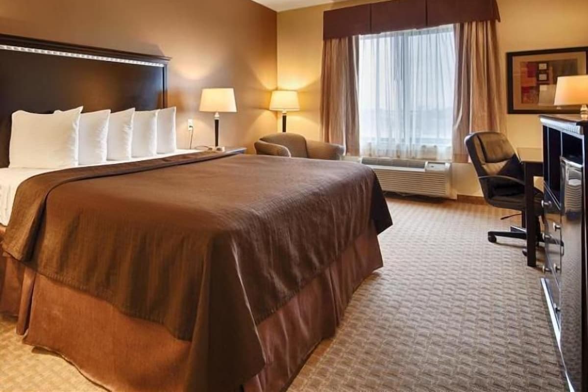 A hotel room with a large bed, a desk, a chair, and a window with curtains.