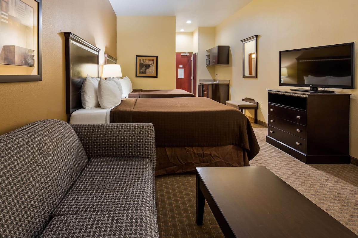 A hotel room with a sofa, two beds, a TV, a dresser, and a framed picture on the wall.