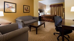 Une chambre d’hôtel avec un canapé à motifs, une petite table, un bureau avec une chaise, un lit recouvert d’une couverture marron et deux tableaux encadrés accrochés au mur.