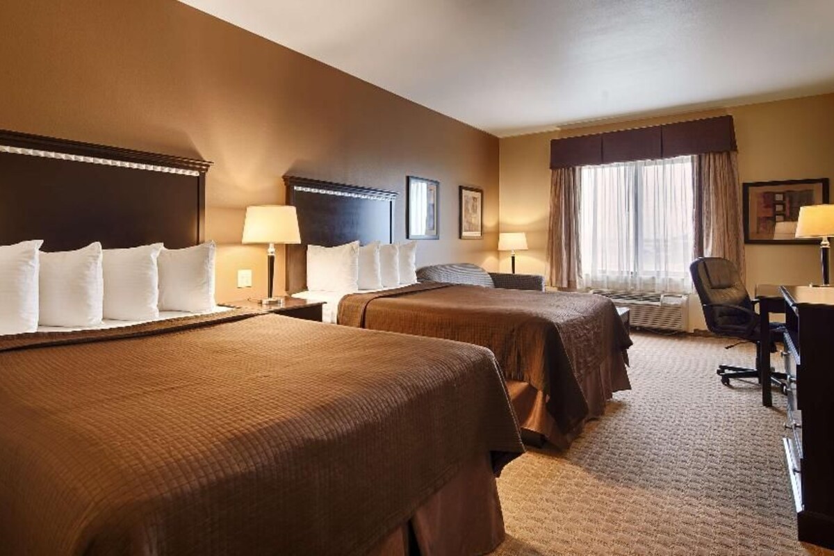 A hotel room with two beds, a desk, a chair, and a window with curtains.