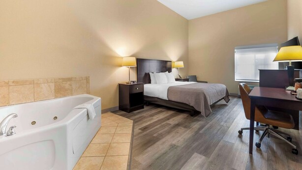 A hotel room with a large bathtub, a bed with two bedside tables, a desk with a chair, and a window. - Quality Inn & Suites Groesbeck North (Groesbeck)