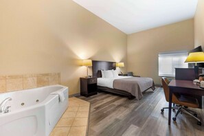 A hotel room with a large bathtub, a bed with two bedside tables, a desk with a chair, and a window.