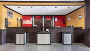 A hotel reception area with a red accent wall, a 'Quality by Choice Hotel' sign, a reception desk, and a check-in counter. - Quality Inn & Suites Groesbeck North (Groesbeck)