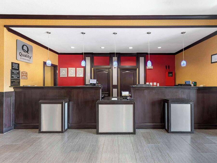 Zona de recepción de hotel con una pared de acento rojo, un letrero que dice 'Quality by Choice Hotel', un mostrador de recepción y un mostrador de registro.