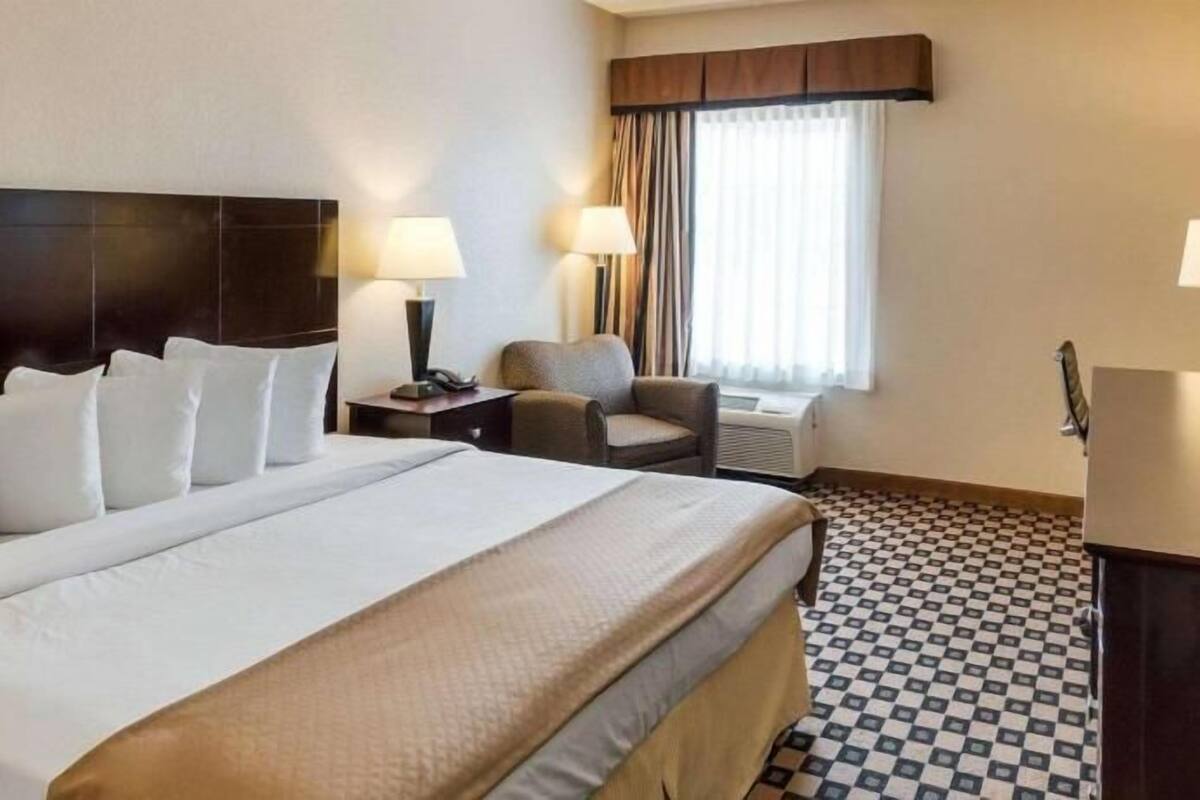 A hotel room with a large bed, a chair, a desk, a TV, and a window with curtains.