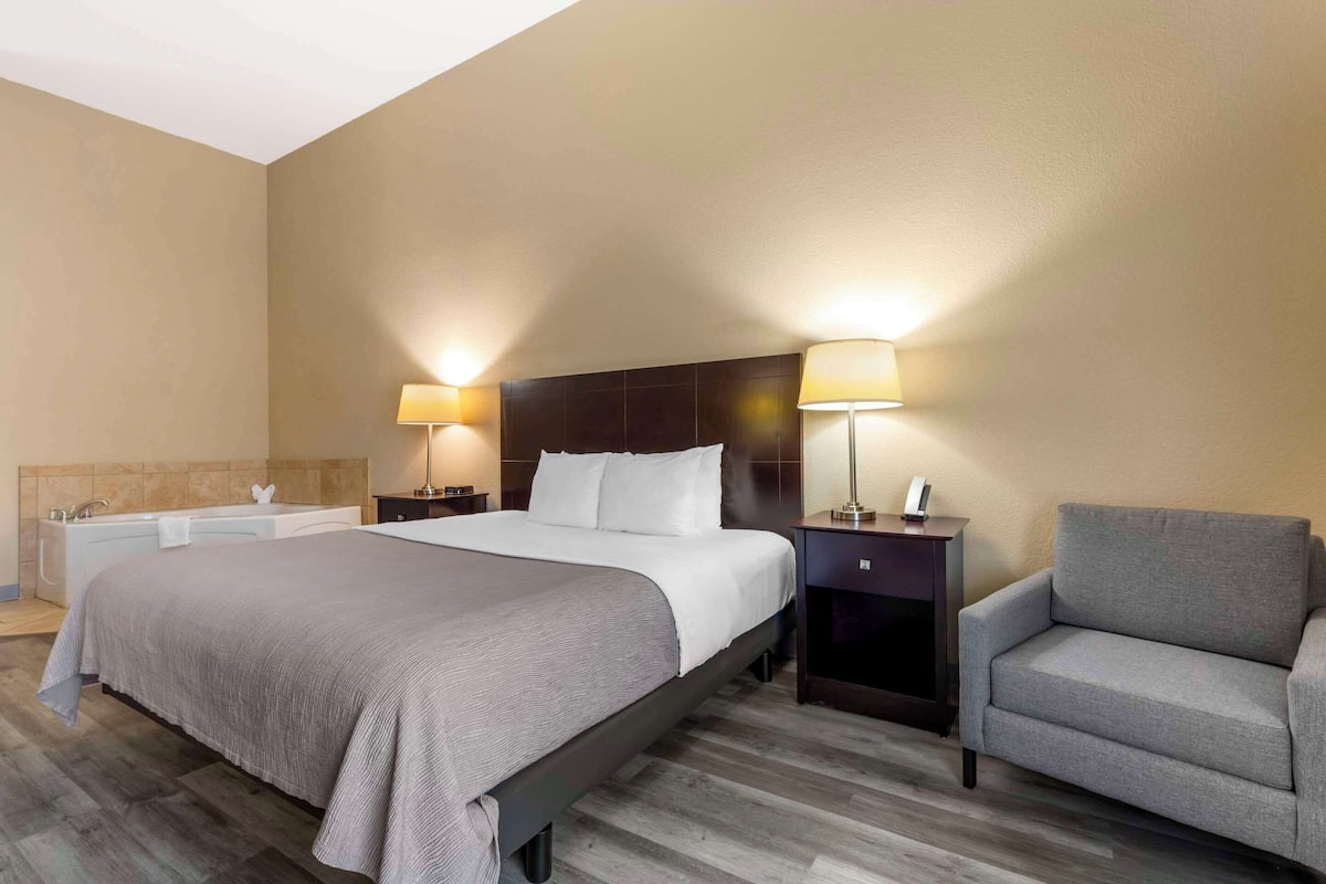 A hotel room with a large bed, two bedside lamps, a chair, a nightstand, and a small table with a lamp.