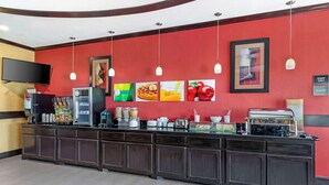 A breakfast bar with a red wall, a flat-screen TV, and various food items. - Quality Inn & Suites Groesbeck North (Groesbeck)