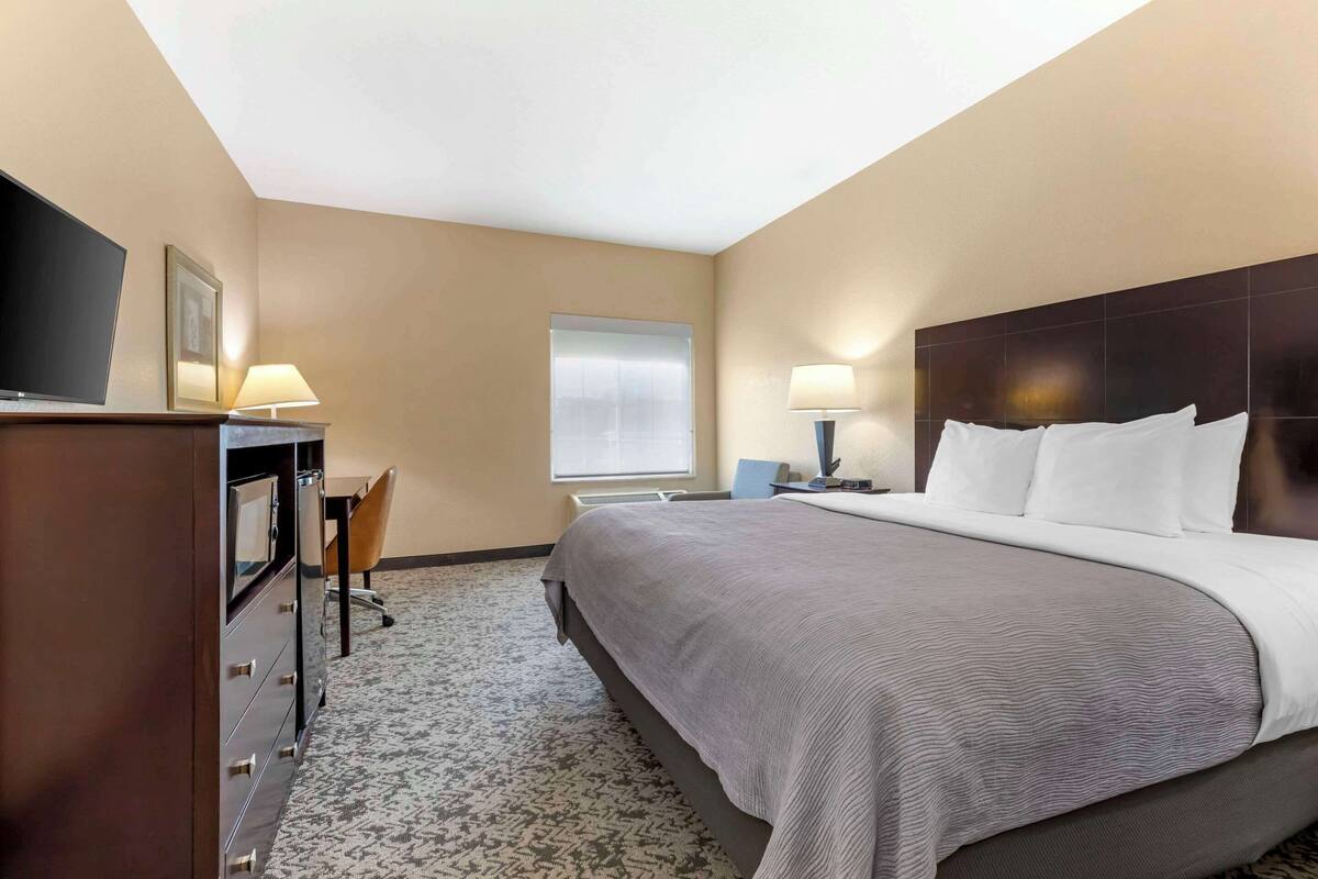 A hotel room with a large bed, a desk with a chair, a TV, and two lamps.