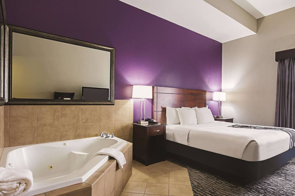 Une chambre d’hôtel avec un grand lit, une salle de bain séparée avec une baignoire et un grand miroir.