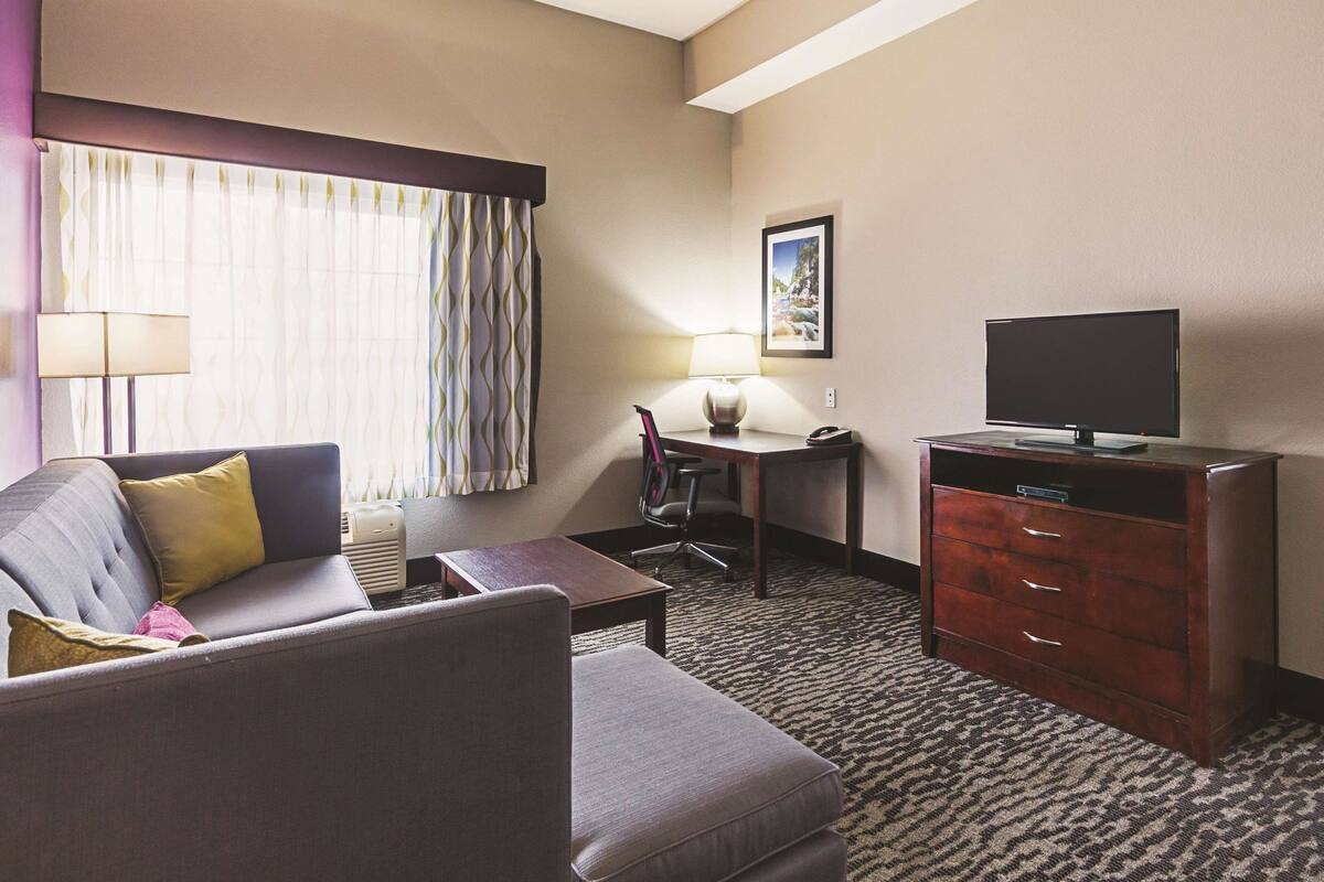 Une chambre d’hôtel avec un canapé, un bureau avec une lampe, un téléviseur posé sur une commode et un sol recouvert de moquette.
