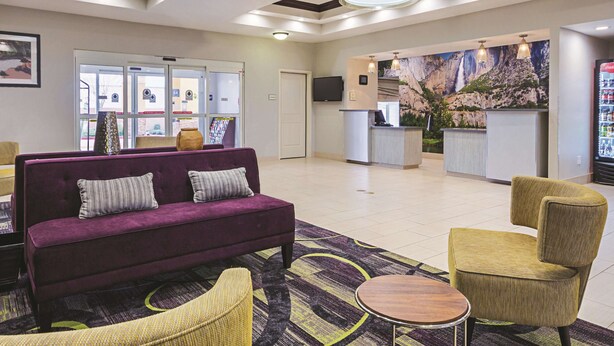 Een hotellobby met een receptiebalie, een paarse bank, gele stoelen en een kamerbreed tapijt met dessin.