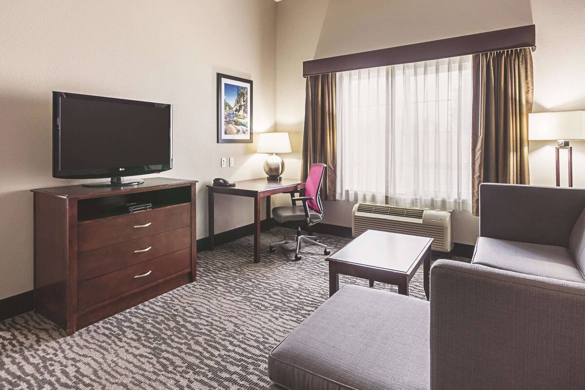 Une chambre d’hôtel équipée d’une télévision à écran plat, d’un bureau avec une lampe, d’une chaise, d’un canapé et d’un sol recouvert de moquette.