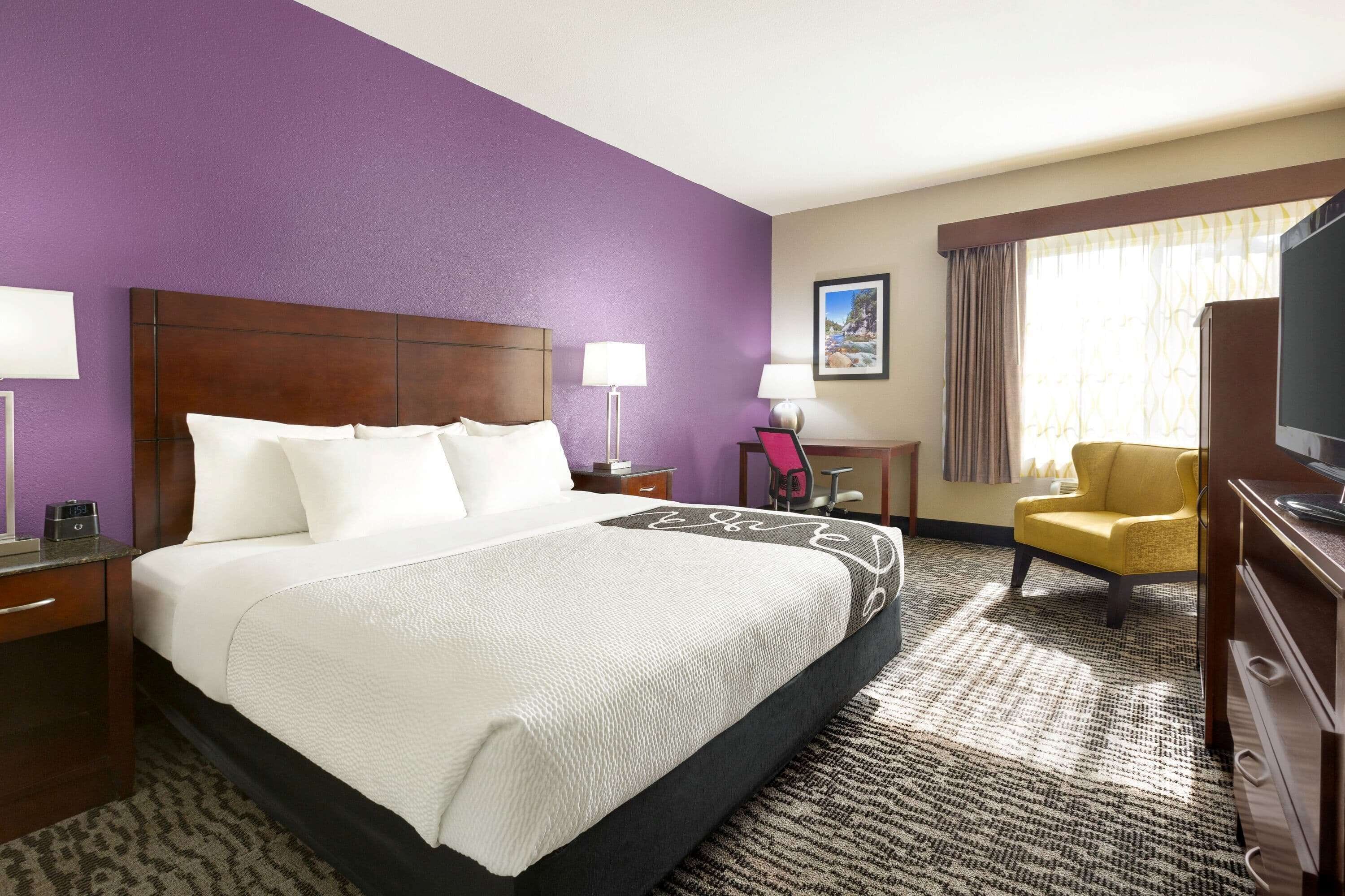 A hotel room with a large bed, a desk, a chair, a television, and a window with curtains.