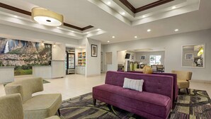 Een ruime lobby met een paarse bank, beige fauteuils, een kamerbreed tapijt met dessin, en een groot wandtapijt met watervalmotieven.