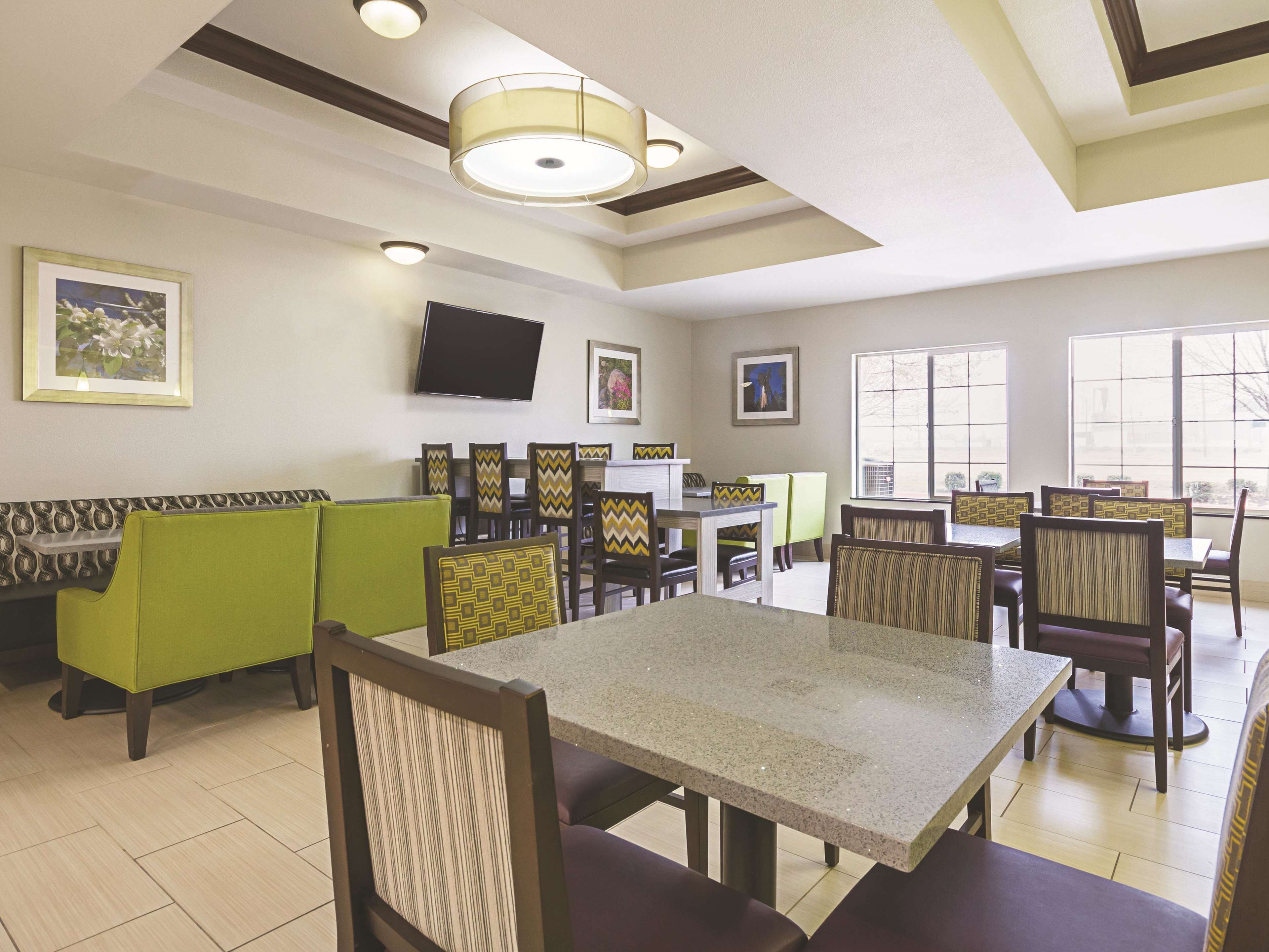A dining area with booths and tables, a flat-screen TV mounted on the wall, and large windows providing natural light.