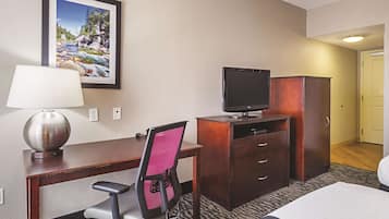 Una habitación de hotel con escritorio, silla, televisor, armario y cama.