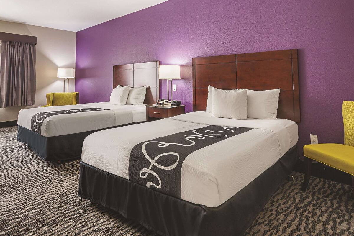 Une chambre d’hôtel avec deux lits, des murs violets et un sol recouvert de moquette.