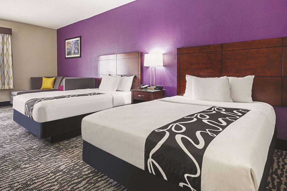 Une chambre d’hôtel avec deux lits, une table de chevet, une lampe et une fenêtre avec des rideaux.
