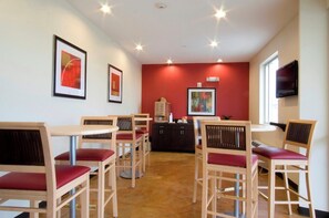 A dining area with wooden tables and chairs, a red accent wall, and artwork on the walls. - Red Roof Inn & Suites Beaumont (Beaumont)