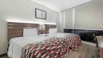Habitación de hotel con dos camas, un ventanal grande, cabecera de madera y un cuadro en la pared.