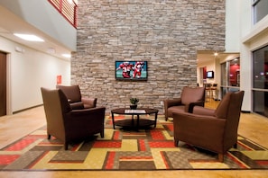 A lobby with a stone wall, two brown armchairs, a small table with a plant, and a television screen. - Red Roof Inn & Suites Beaumont (Beaumont)
