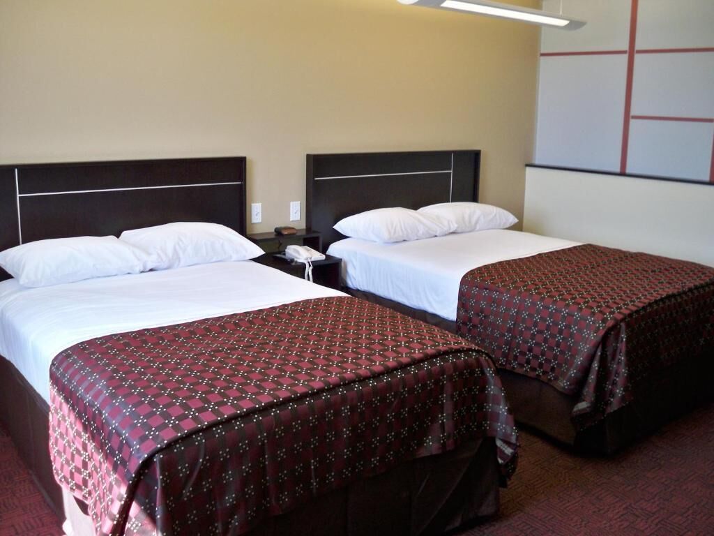 Ein Hotelzimmer mit zwei Betten, jeweils mit einem gemusterten Bettüberwurf, einem Nachttisch mit Telefon und einer Wand mit geometrischem Dekor.