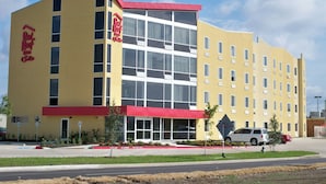 A hotel with a red and yellow facade, multiple windows, and a parking lot with a few cars. - Red Roof Inn & Suites Beaumont (Beaumont)