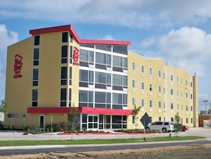 A hotel with a red and yellow facade, multiple windows, and a parking lot with a few cars. - Red Roof Inn & Suites Beaumont (Beaumont)