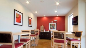 A dining area with wooden tables and chairs, a red accent wall, and artwork on the walls. - Red Roof Inn & Suites Beaumont (Beaumont)