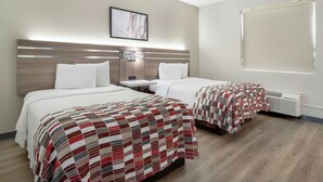 Une chambre d’hôtel avec deux lits, une table de chevet, une lampe fixée au mur et une fenêtre avec des stores.