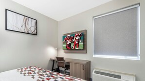 A bedroom with a bed, a desk, a chair, a painting, a window, and an air conditioner. - Red Roof Inn & Suites Beaumont (Beaumont)