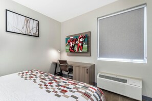 A bedroom with a bed, a desk, a chair, a painting, a window, and an air conditioner. - Red Roof Inn & Suites Beaumont (Beaumont)
